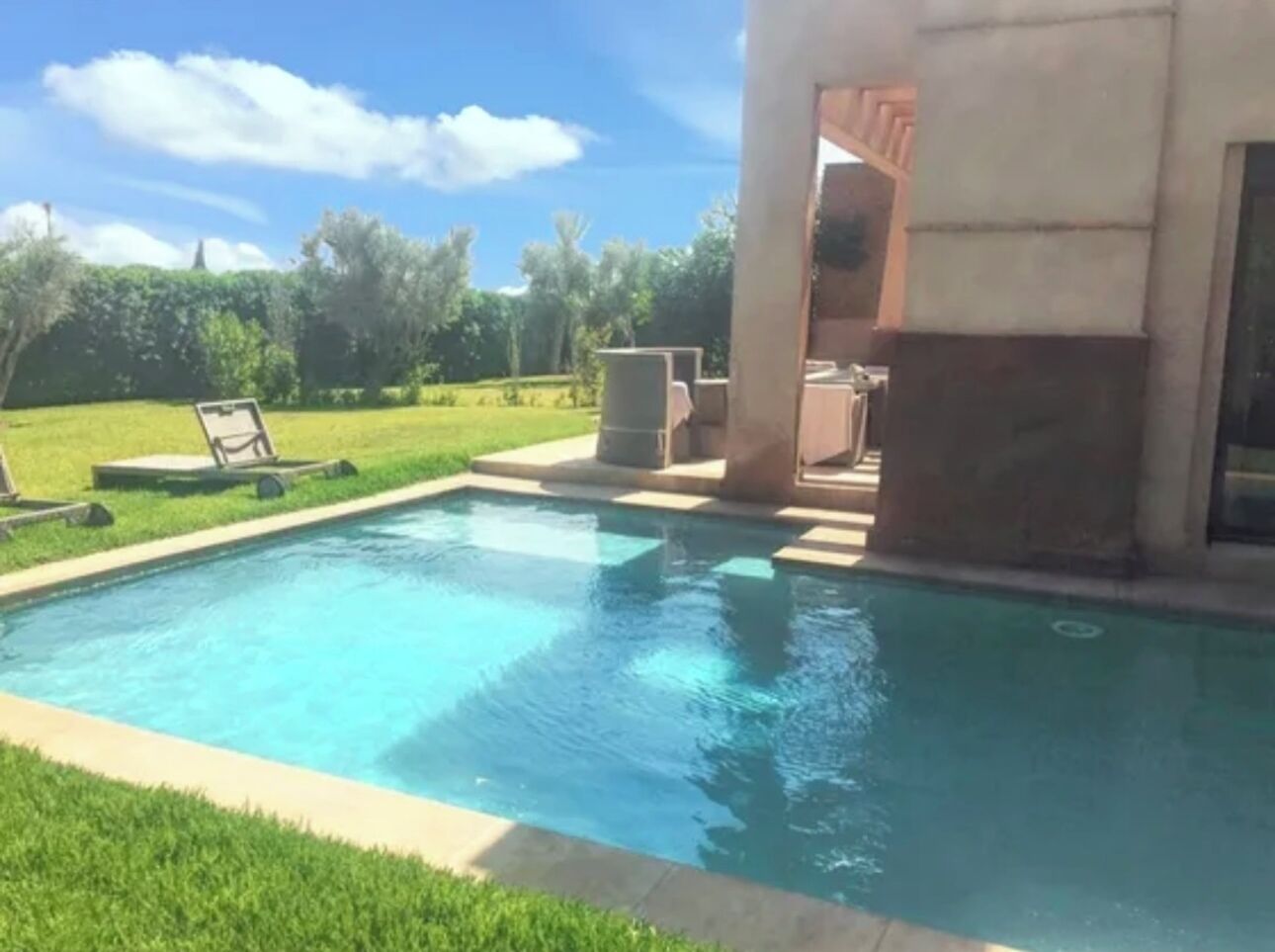 Una piscina rectangular con agua cristalina azul, rodeada por un césped cuidado y un patio con mobiliario exterior.