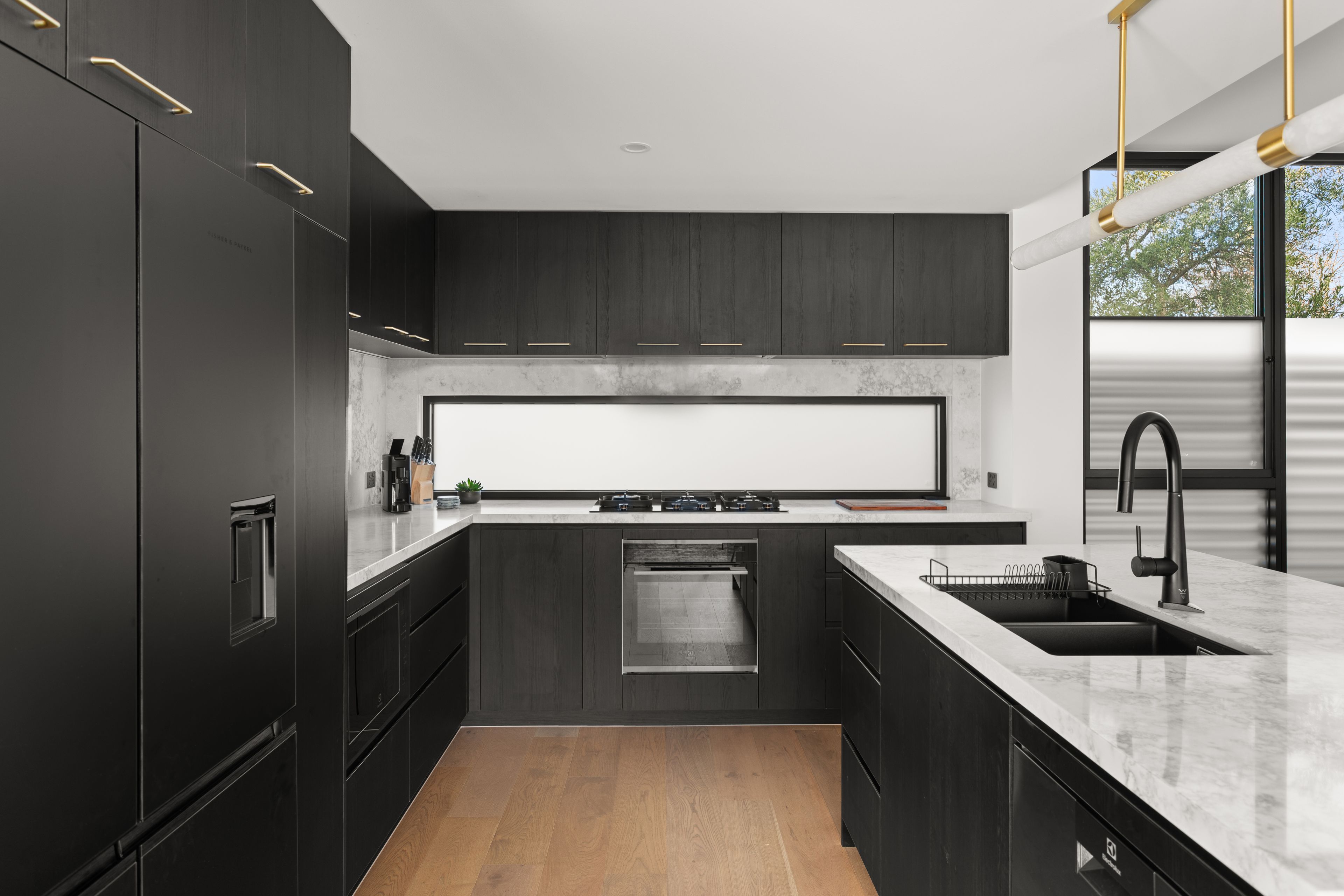 A modern kitchen with dark cabinetry, a stainless steel oven, and a large window providing natural light.