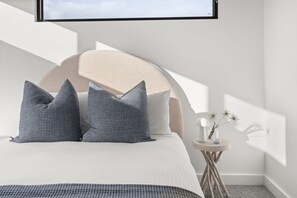Une chambre à coucher moderne avec un lit, des oreillers, une table de chevet et un téléviseur fixé au mur.