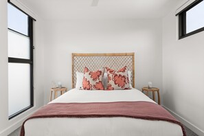 Ein Schlafzimmer mit einem Bett, zwei Nachttischen, einem Fenster und einem Kopfteil mit Gewebemuster.