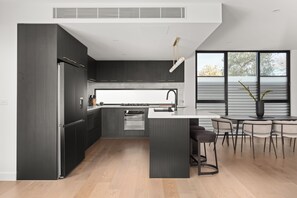 A modern kitchen with dark cabinetry, a central island, and a dining area with a table and chairs. - Sierra Vista Pet Friendly Holiday Home in Rosanna (Rosanna)