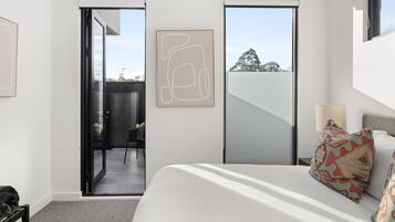 A modern bedroom with a large bed, a sliding door to a balcony, and a framed abstract artwork on the wall.