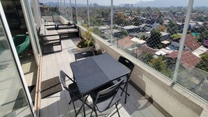 Un balcón con mesa y sillas, con vista a una zona residencial con casas y montañas a lo lejos.