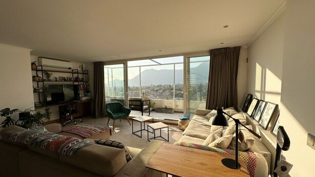 Una sala de estar moderna con sofá, sillón y mesa de centro, televisor y balcón con vista a la montaña.
