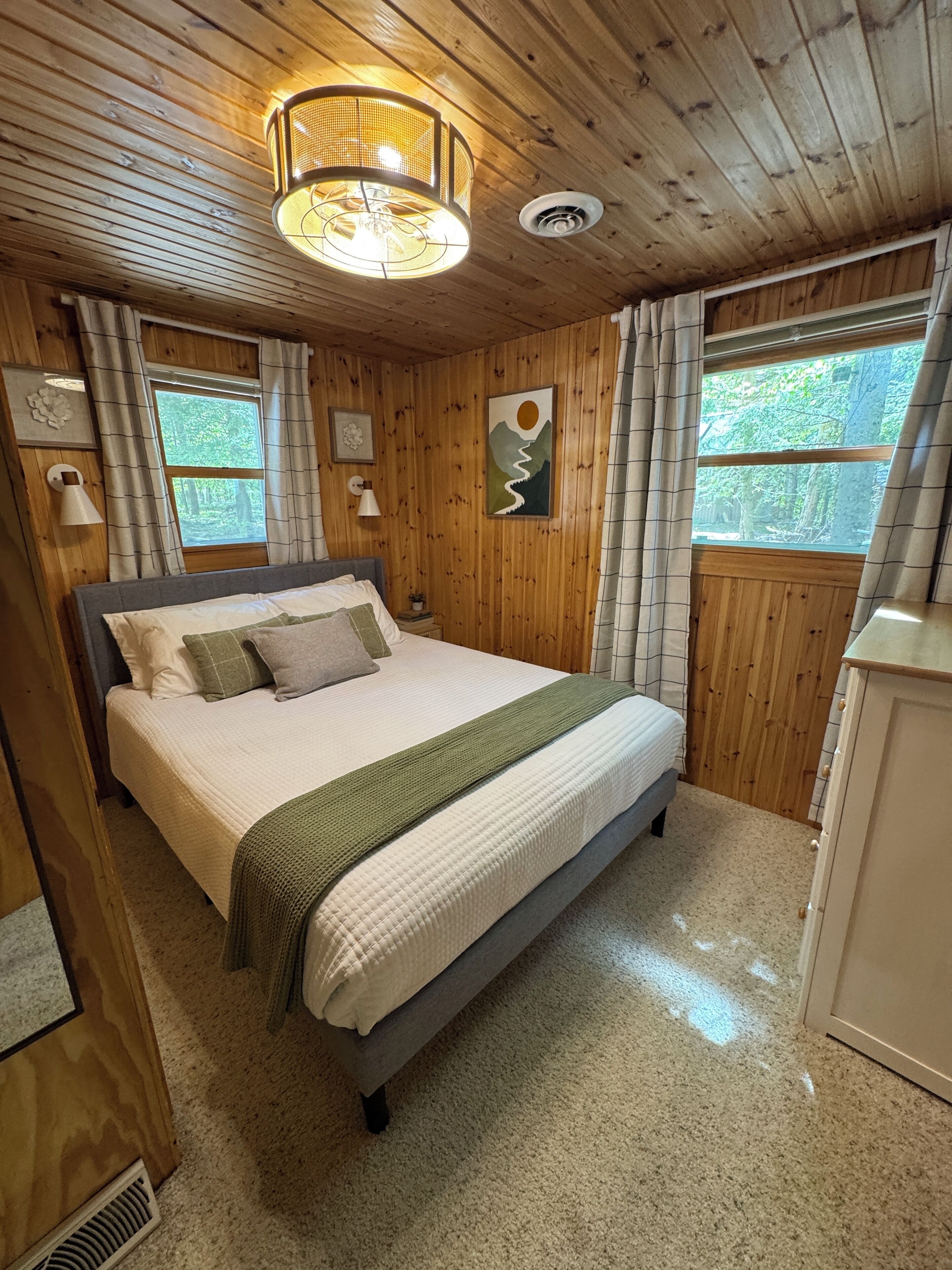 A wooden-paneled bedroom with a bed, a ceiling light, and a window with curtains.