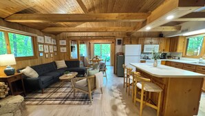 Een ruime woonkamer met een donkergroene bank, een houten salontafel, en een eethoek met houten stoelen en een wit kookeiland.