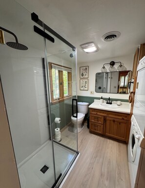 A modern bathroom with a glass shower enclosure, a toilet, a sink, and a washing machine.