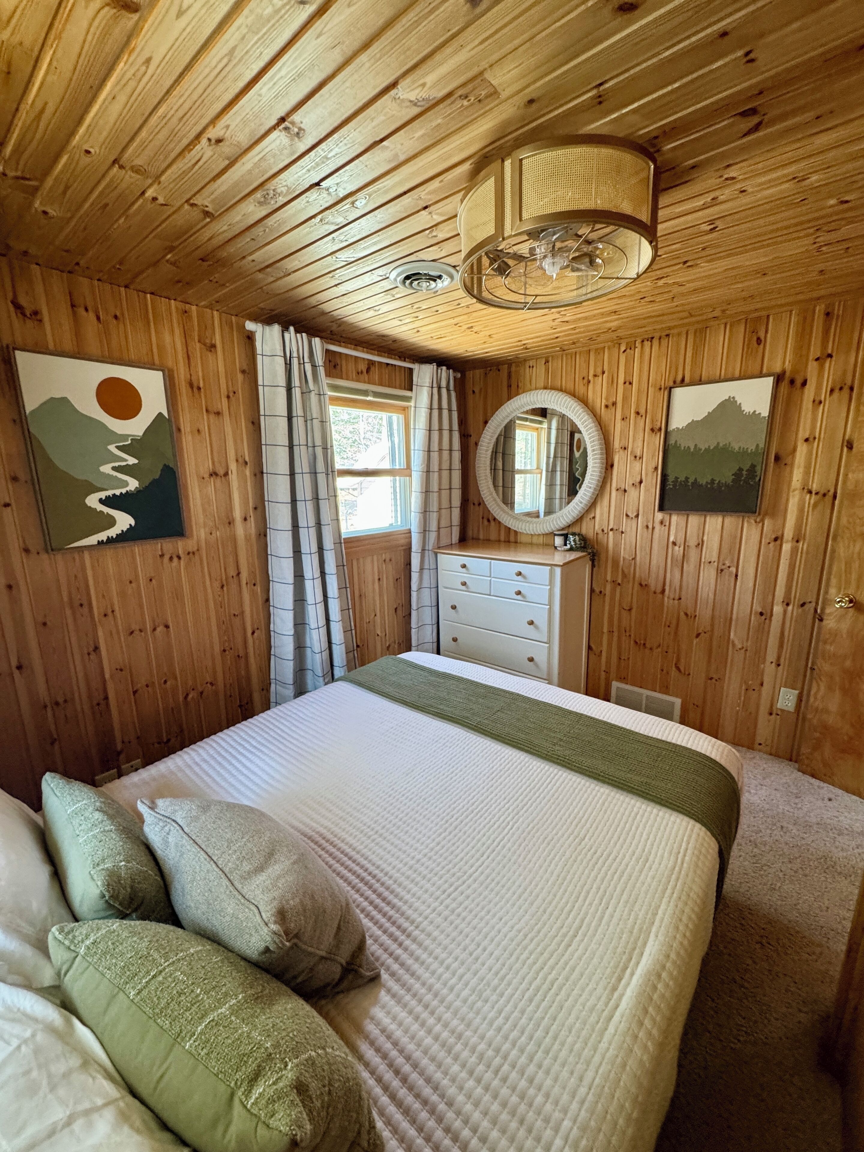 A wooden-paneled bedroom with a bed, dresser, and a ceiling fan.