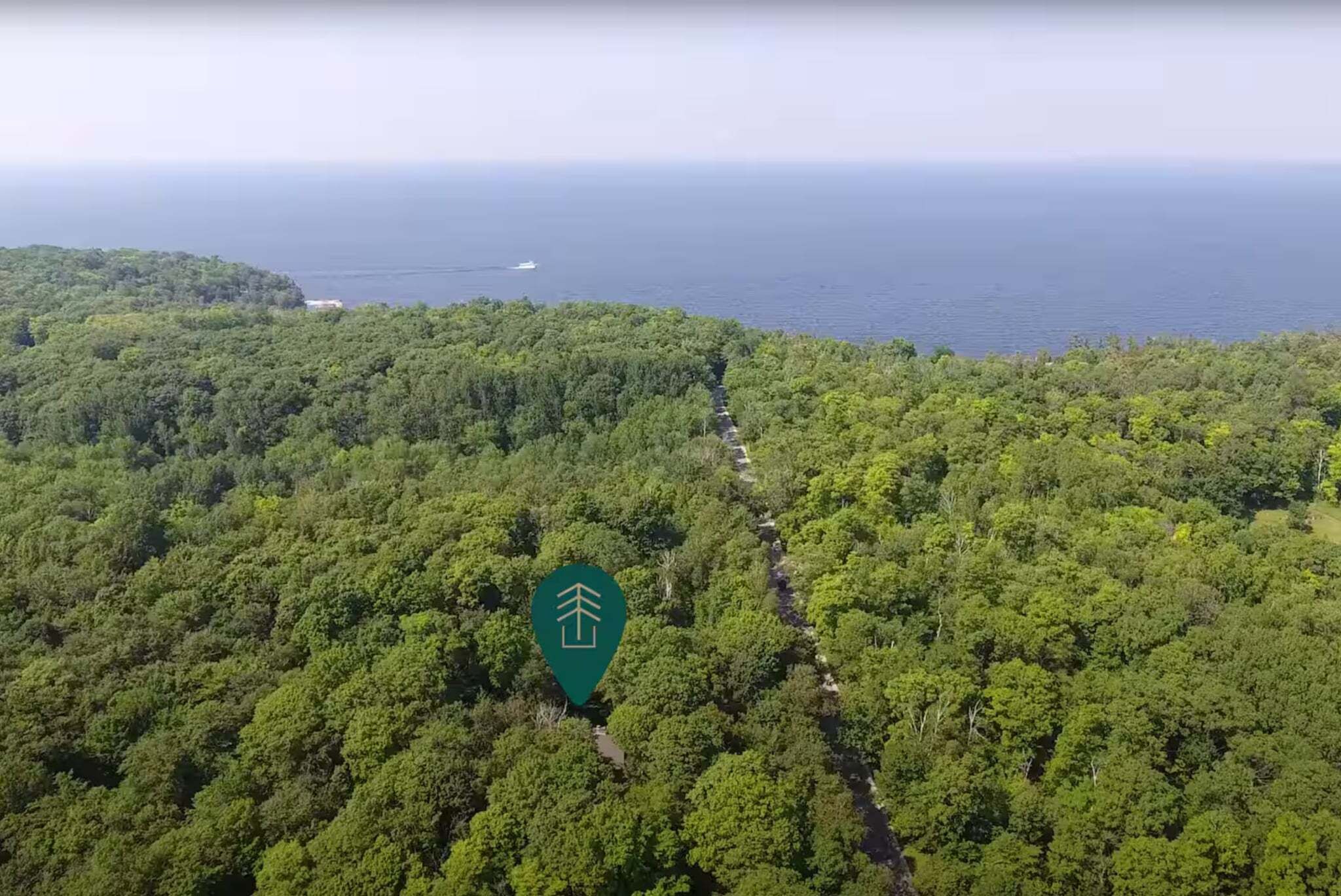 Une vue aérienne d’une forêt dense, avec un sentier bien tracé qui mène à une zone côtière.