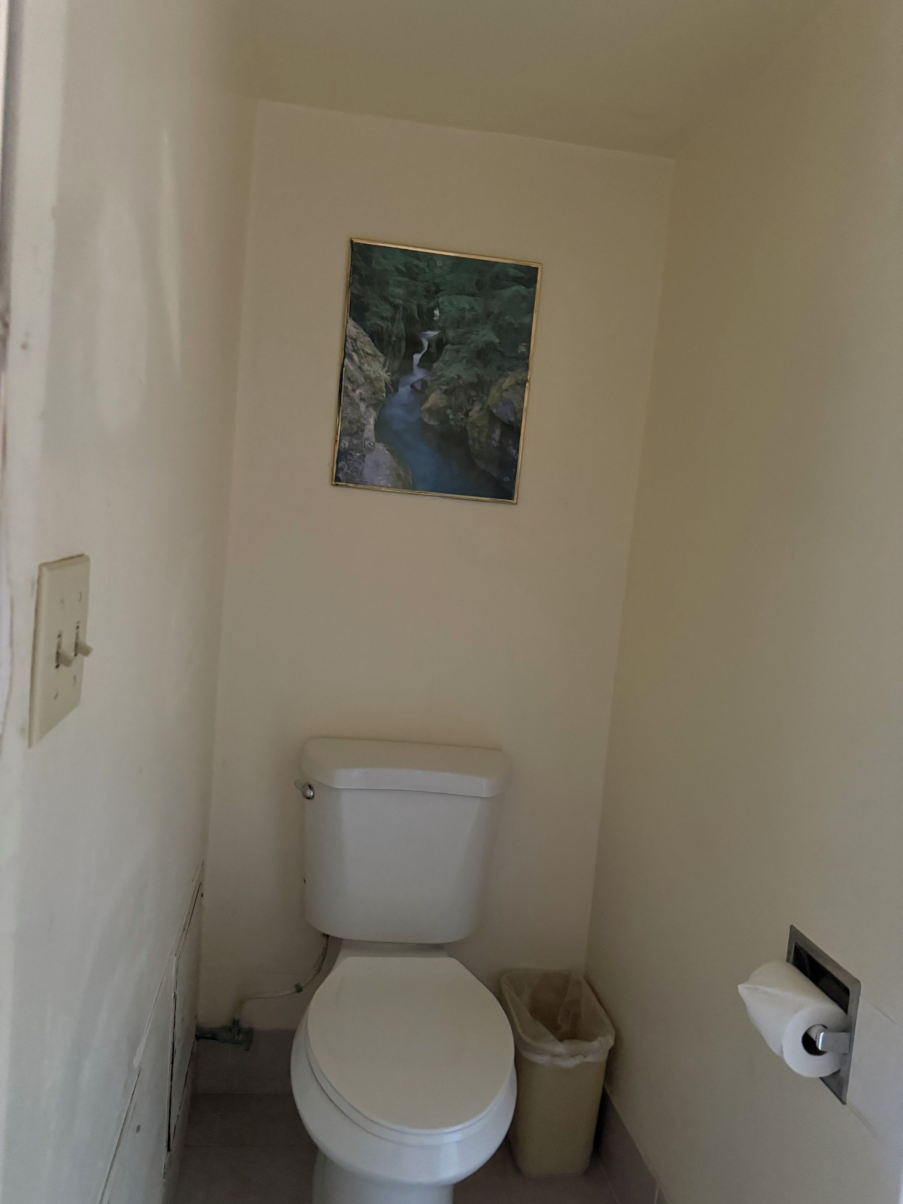 Un baño pequeño y estrecho con un inodoro blanco, un cubo de basura y un dispensador de papel higiénico.