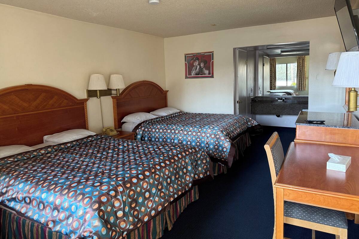 A hotel room with two beds, a desk, a mirror, and a bathroom visible through an open door.
