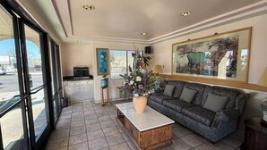 Un salon spacieux avec un grand canapé, une table basse et une plante en pot. Un tableau est accroché au mur et il y a une fenêtre avec des stores.