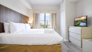 Une chambre d’hôtel avec un lit, une télévision, une fenêtre avec des rideaux et une vue sur des immeubles.