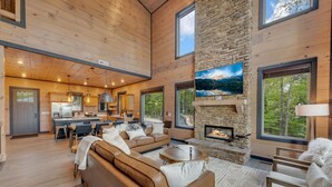 A spacious living area with a stone fireplace, large windows, and a cozy seating arrangement. - New/Theater/Indoor pool/Hot tub/Fire pit/Arcades/View (Sevierville)