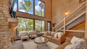 A spacious living area with a large window, a stone wall, a wooden staircase, and a cozy seating arrangement. - New/Theater/Indoor pool/Hot tub/Fire pit/Arcades/View (Sevierville)