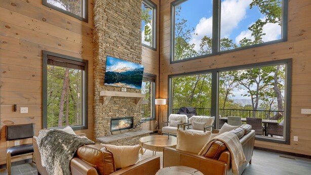 A spacious living room with a stone fireplace, large windows, and a cozy seating area. - New/Theater/Indoor pool/Hot tub/Fire pit/Arcades/View (Sevierville)