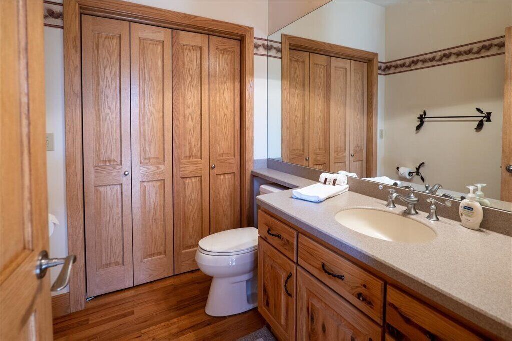 Une salle de bain avec des meubles en bois, des toilettes blanches, un lavabo avec un miroir et des articles de toilette.