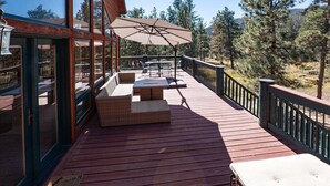 Una terraza de madera con mobiliario exterior, que incluye una mesa y sillas, y un gran paraguas.