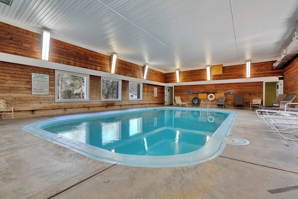 An indoor swimming pool with wooden walls, ceiling lights, and lounge chairs.