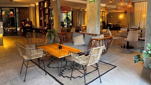 A modern, well-lit lounge area with a wooden table, wicker chairs, and a large potted plant. - Tuk Tulum by Marea (Tulum)