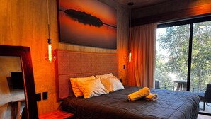 A modern hotel room with a large bed, wooden headboard, and a painting of a sunset over water. - Tuk Tulum by Marea (Tulum)