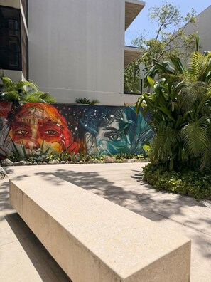 A modern outdoor area with a concrete bench, a colorful mural, and lush greenery.
