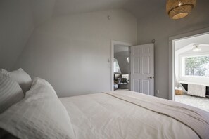 A bedroom with a large bed, a door leading to a bathroom, and a view of the outdoors.