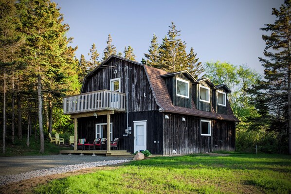 A rustic wooden house with a balcony, surrounded by a forest.