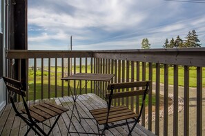 A wooden deck with a table and two chairs, overlooking a grassy area with trees.