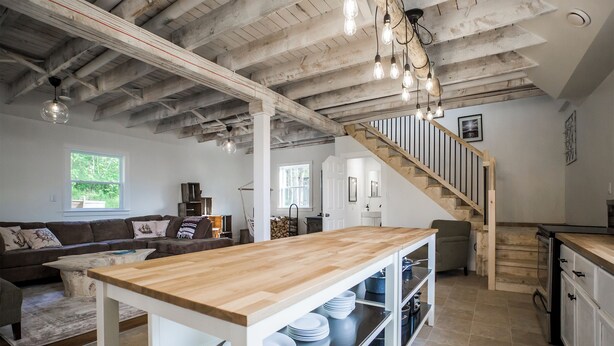 A spacious kitchen with a wooden table, white cabinets, and a staircase leading to a loft. - Ultra Private Oceanfront Cottage with Sunset Views (Middleton)