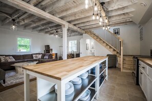 A spacious kitchen with a wooden table, white cabinets, and a staircase leading to a loft. - Ultra Private Oceanfront Cottage with Sunset Views (Middleton)