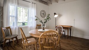 A dining area with a round wooden table, four wooden chairs, a vase with flowers, a wall clock, and a pendant light. - Ultra Private Oceanfront Cottage with Sunset Views (Middleton)