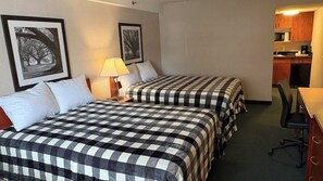 A hotel room with two beds, a desk, a chair, a lamp, and a kitchenette.