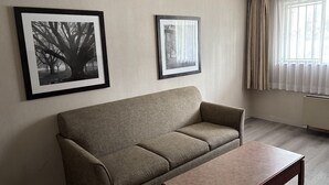 A living room with a sofa and a coffee table, two framed pictures on the wall, and a window with curtains.