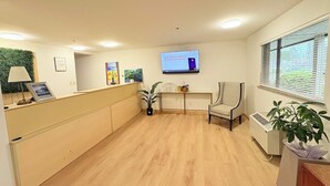 A reception area with a wooden floor, a reception desk, a chair, a TV screen, and a window with blinds.