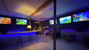 A bar area with multiple screens displaying various content, bar stools, and a wooden ceiling structure.