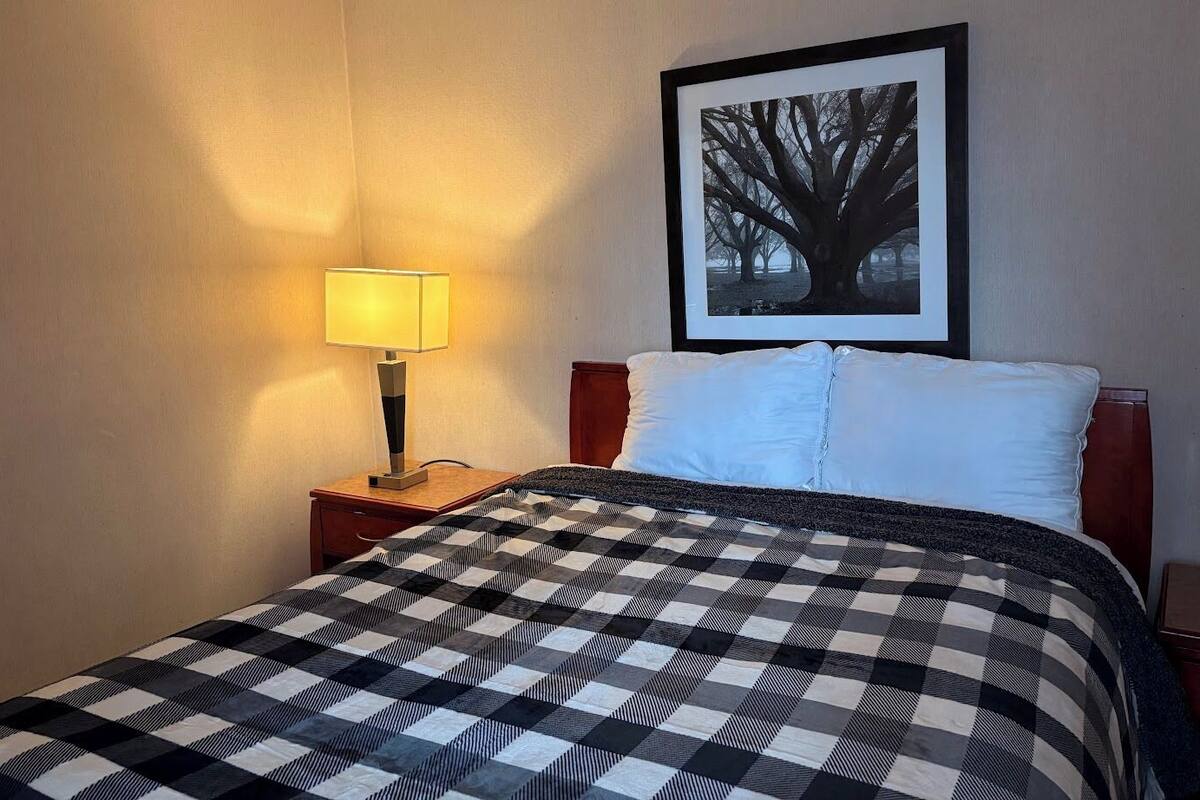 A hotel room with a bed, a nightstand with a lamp, and a framed picture on the wall.