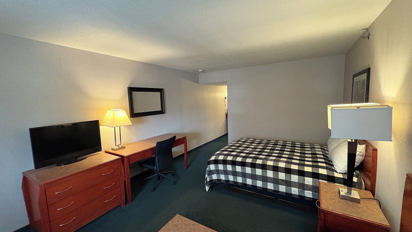 Habitación de hotel con cama, escritorio con silla, televisor y lámpara.