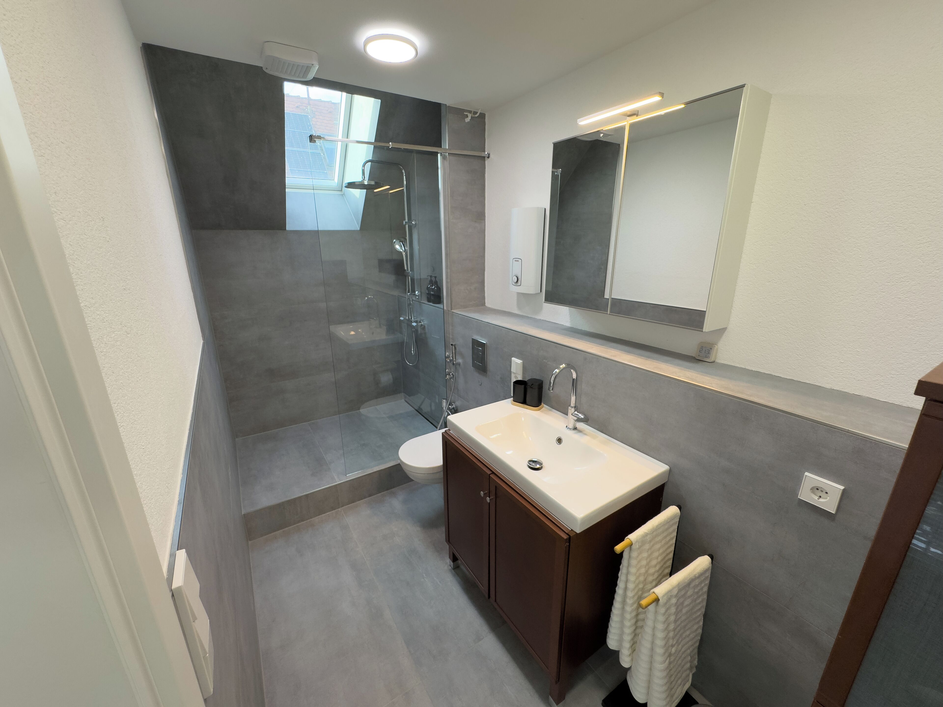 Une salle de bain moderne avec une douche à parois de verre, un lavabo blanc et un miroir au-dessus du lavabo.