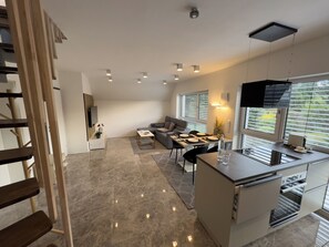 Eine moderne Küche mit Einbauofen, ein Essbereich mit Tisch für vier Personen und ein Wohnzimmer mit Sofa und Fernseher.