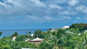 A coastal view with houses, palm trees, and the ocean under a cloudy sky. - 2-Bedroom Apartment - Les Jardins de Delgrès: Set in lush greenery, with views of the sea and mountains (Trois-Rivières)