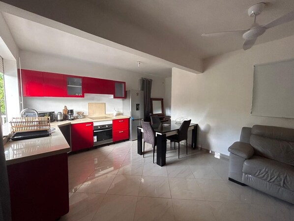 Uma cozinha moderna com armários vermelhos, um espaço de refeições com mesa e cadeiras, e um sofá cinza numa sala de estar ampla.