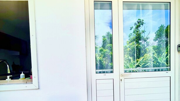 A room with a sliding door leading to a balcony, a small window, and a doormat with a house symbol. - 2-Bedroom Apartment - Les Jardins de Delgrès: Set in lush greenery, with views of the sea and mountains (Trois-Rivières)