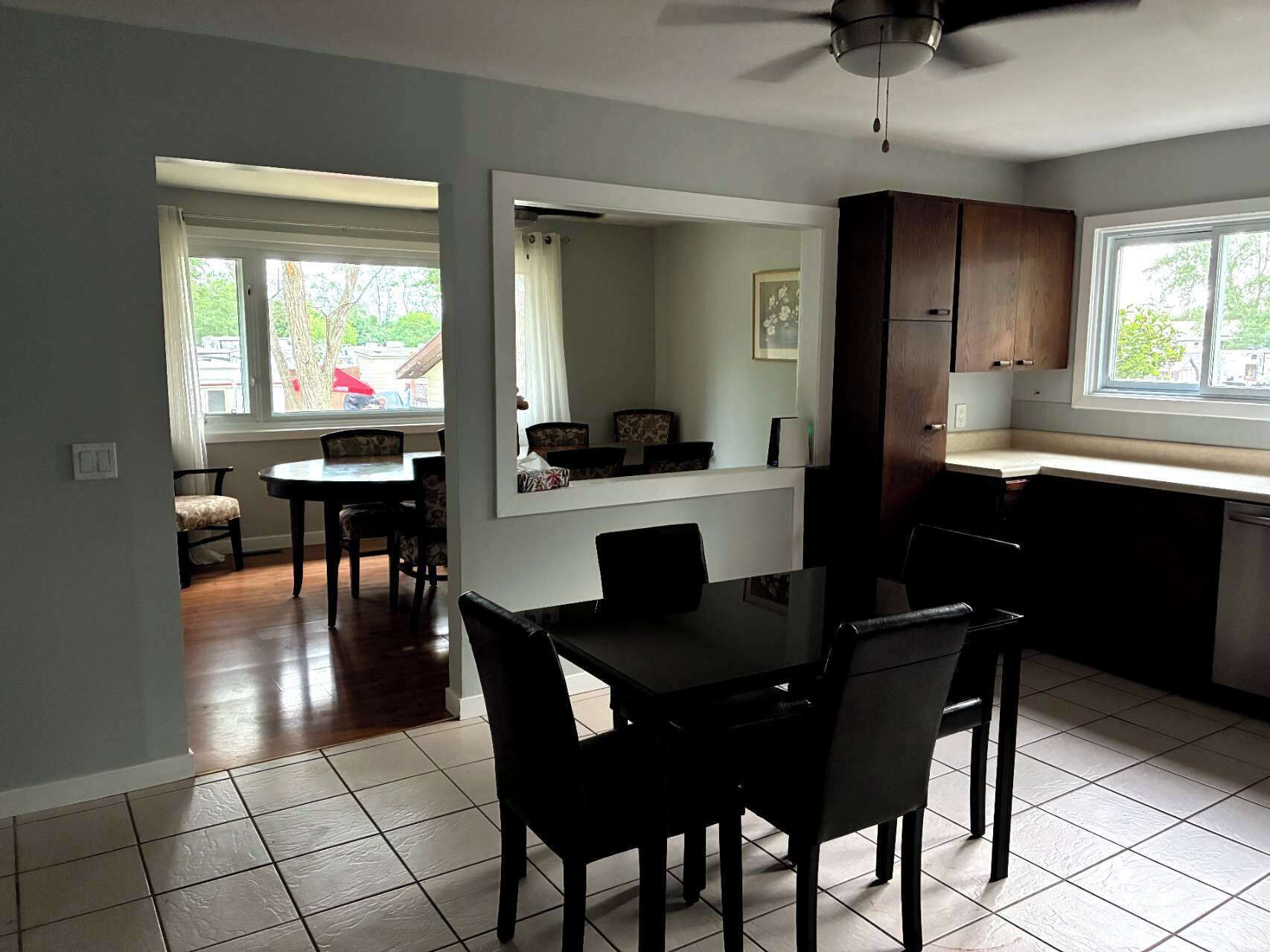 A modern kitchen with dark cabinetry, a dining area with a table and chairs, and large windows providing natural light.