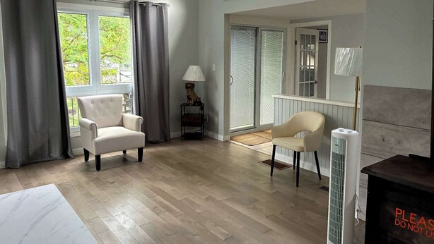 A spacious room with a large window, a chair, a small table with a lamp, and a radiator.