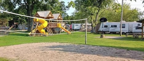 A playground with a yellow slide and a wooden playhouse.