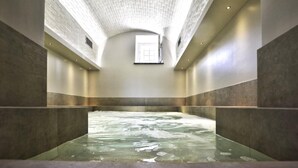 Ein Spa mit einer großen, rechteckigen Whirlpoolwanne in der Mitte, umgeben von Steinwänden und einer hohen, gewölbten Decke.