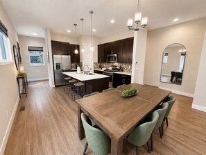 Een moderne keuken met een centraal eiland, barkrukken, een eettafel met stoelen en hanglampen.