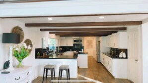 A modern kitchen with white cabinetry, a central island, and a dining area with two stools. - Spacious 5-bedroom house with a peaceful view in Arroyo Grande (Arroyo Grande)