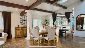 A spacious dining area with a round table and six chairs, a large wall clock, and a view of the outdoors through large windows. - Spacious 5-bedroom house with a peaceful view in Arroyo Grande (Arroyo Grande)